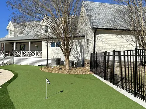 Backyard putting green with a flag beside a white house and a black fence