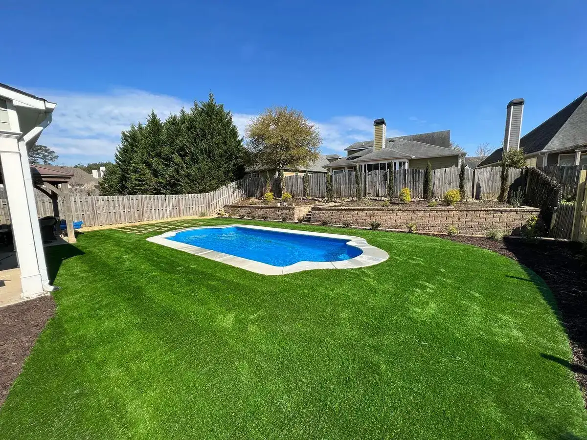 Backyard swimming pool surrounded by turf, stone wall and planting