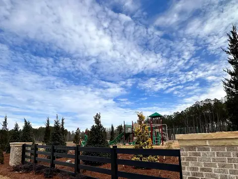 Black rail fence and brick columns beside a community playground with new plantings