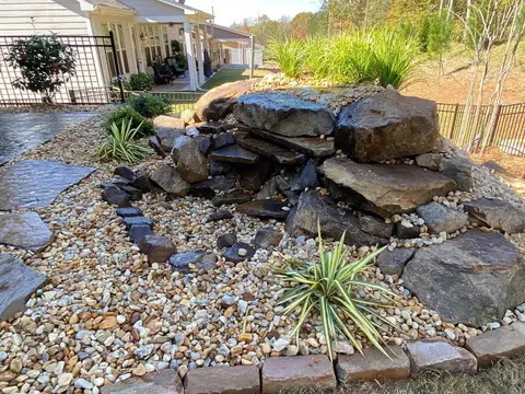 Boulder waterfall with river rock, a flagstone patio and brick edging in a backyard