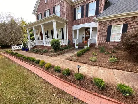 Boxwoods and pine-straw beds with a brick edge along a front walk and covered porch