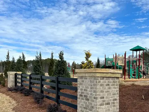 Brick pier and black fence by a community playground, with shrubs in a pine-straw bed