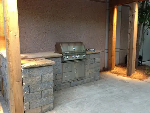 Built-in grill and cabinets in a stone-faced outdoor kitchen under a timber frame