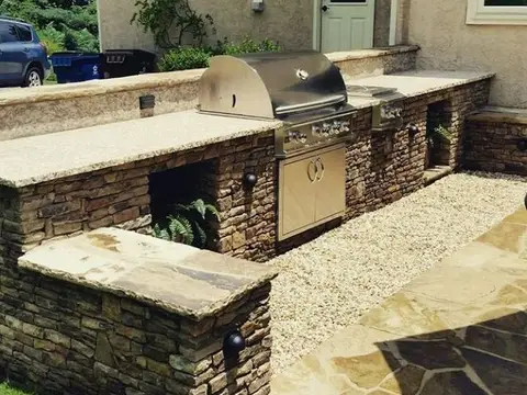 Built-in outdoor grill and counter in stacked stone with a flagstone patio and gravel path