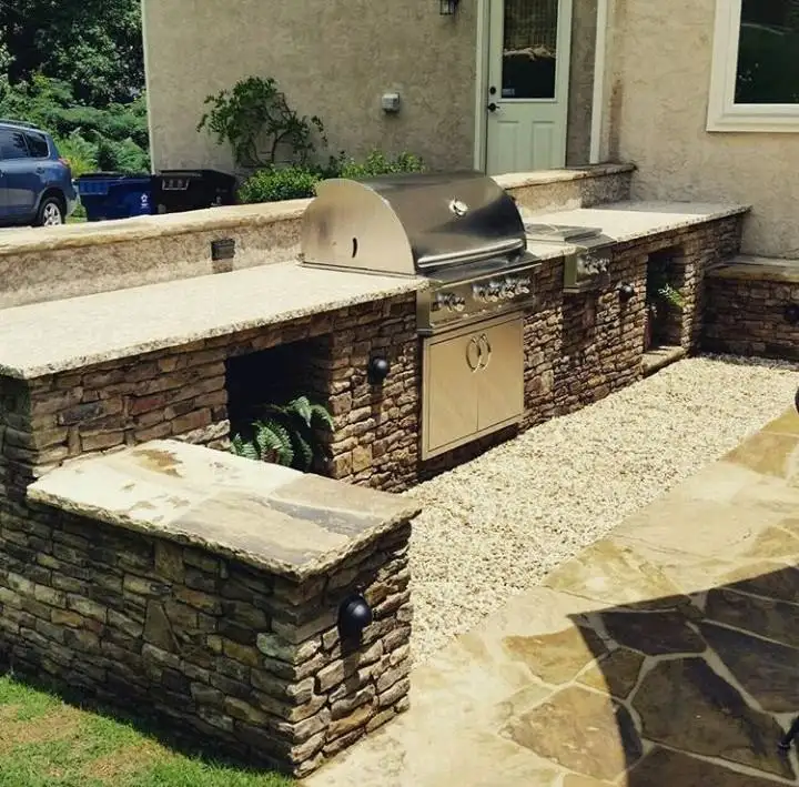 Built-in outdoor grill and counter in stacked stone with a flagstone patio and gravel path