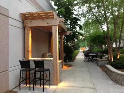 Cedar pergola bar with stools and a stone-faced counter along a sidewalk