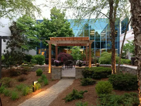 Courtyard seating and a pergola behind landscaped beds outside an office building