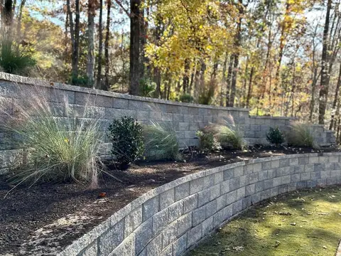 Curved block retaining wall with ornamental grasses above a lawn