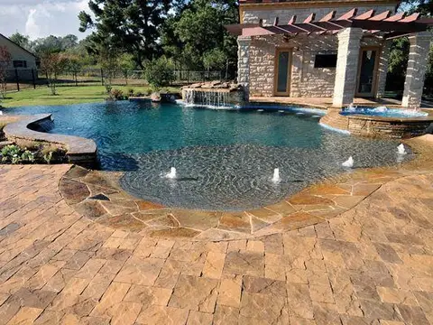 Freeform pool with a paver deck, waterfall and stone cabana