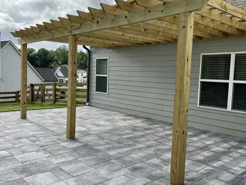 Gray paver patio with a timber pergola beside a house