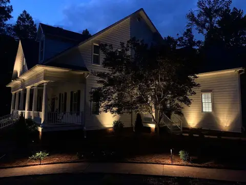 Home with an uplit porch and glowing trees at dusk