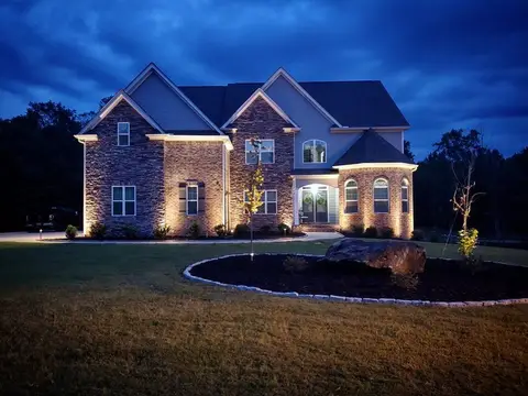 Home with landscape uplighting and a lit border around a planted bed at dusk