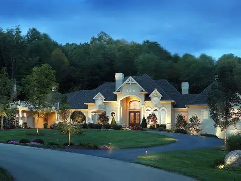 Large home with landscape lighting along a curved driveway at dusk