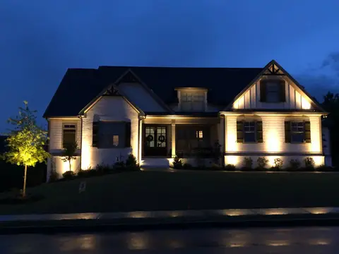 Modern farmhouse with uplighting on its gables and trees at dusk