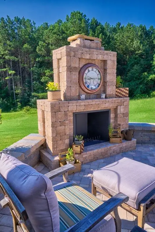 Paver outdoor fireplace with a clock, flowers and cushioned chairs