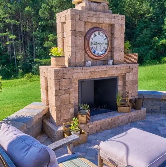 Paver outdoor fireplace with a clock, flowers and cushioned chairs