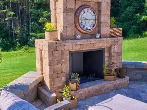 Paver outdoor fireplace with a clock, flowers and cushioned chairs