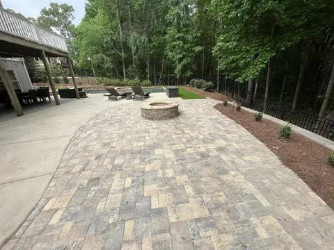 Paver patio extending to a fire pit beside a wooded backyard