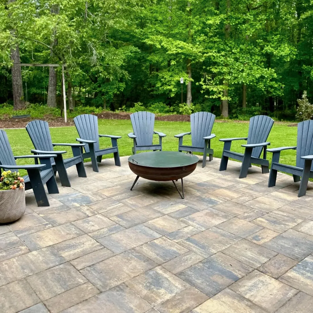 Paver patio with a fire pit and Adirondack chairs overlooking a lawn