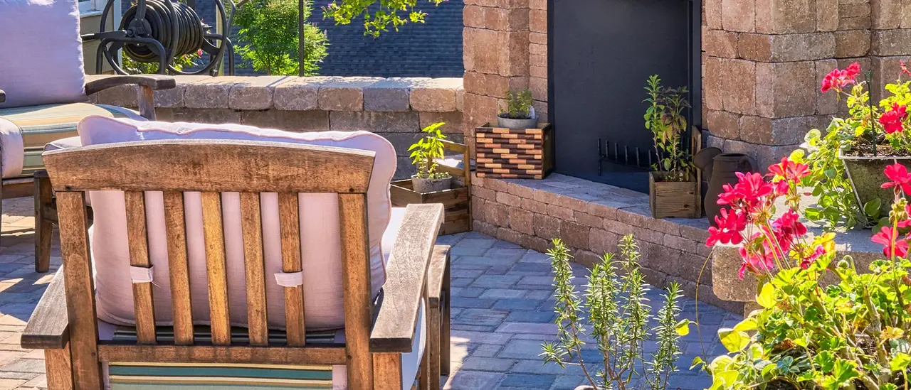 Brick paver patio with a stone fireplace, a wooden armchair and flowering planters