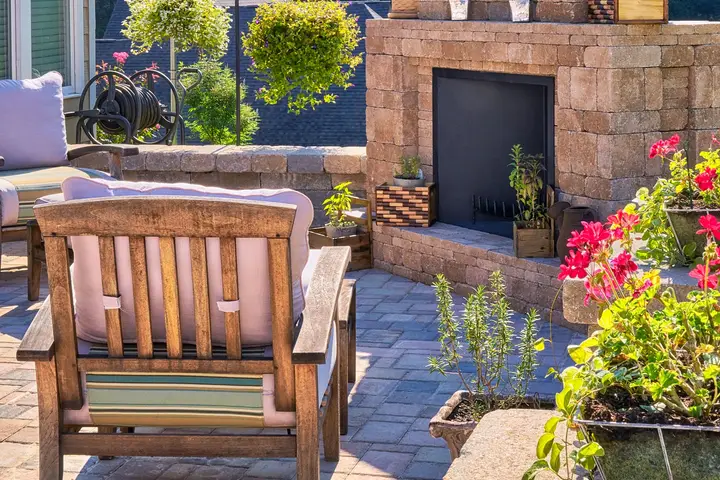 Brick paver patio with a stone fireplace, a wooden armchair and flowering planters