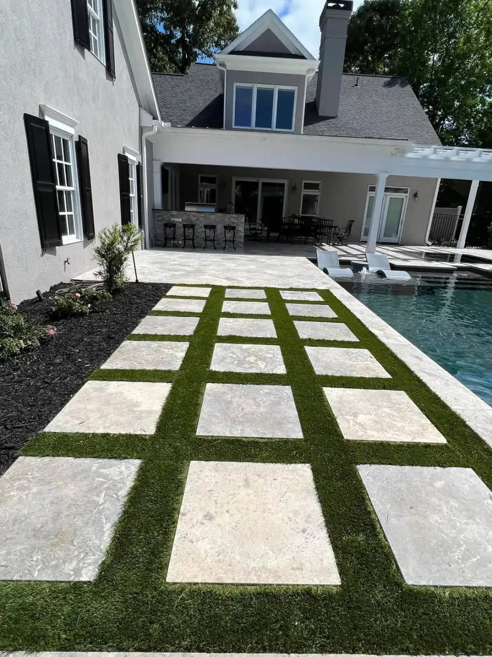 Paver patio set in turf beside a pool and covered patio