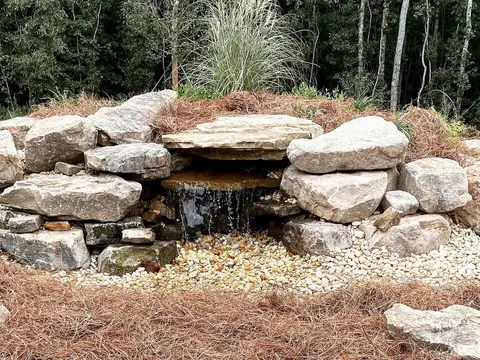 Pondless waterfall over stacked boulders with river rock and pine straw