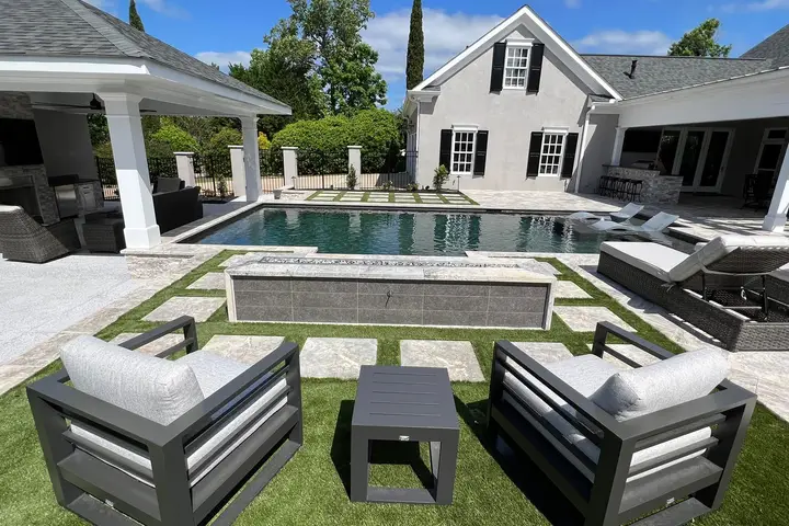 Backyard pool surrounded by turf and stone pavers, with lounge seating and a covered outdoor kitchen