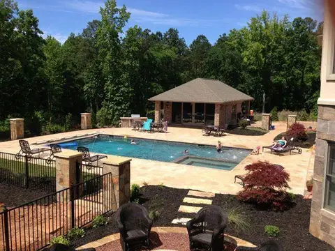 Pool with a cabana, paver deck and landscaped beds surrounded by woods