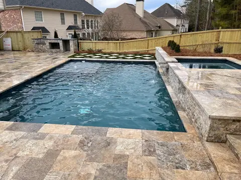 Rectangular pool with a raised spa wall and a travertine deck beside a built-in outdoor kitchen