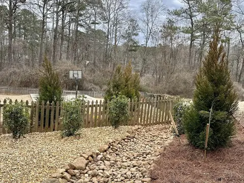Rock-lined drainage channel with young evergreens beside a wooden fence