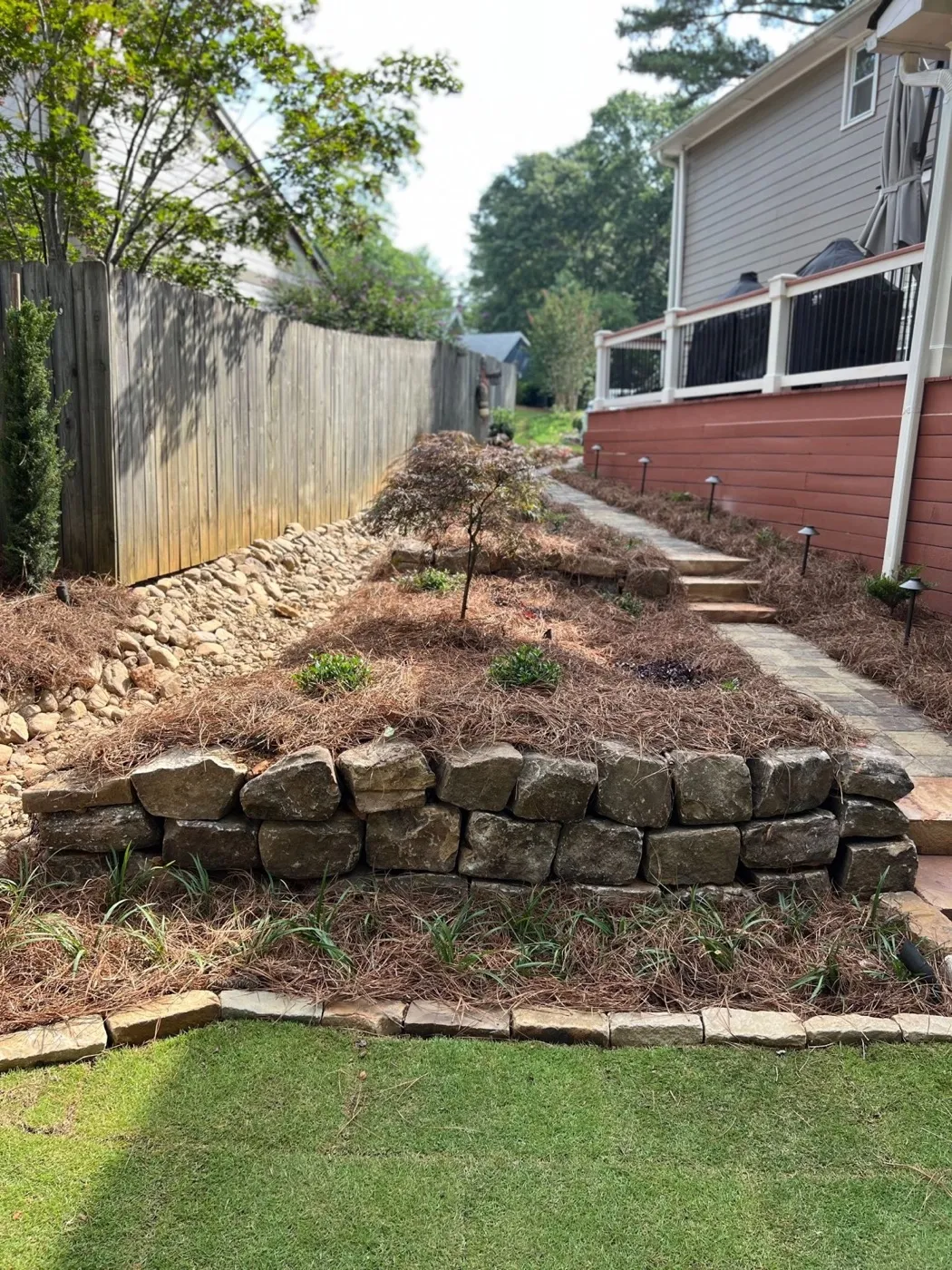 Tiered natural stone retaining wall with pine-straw beds, steps and path lights