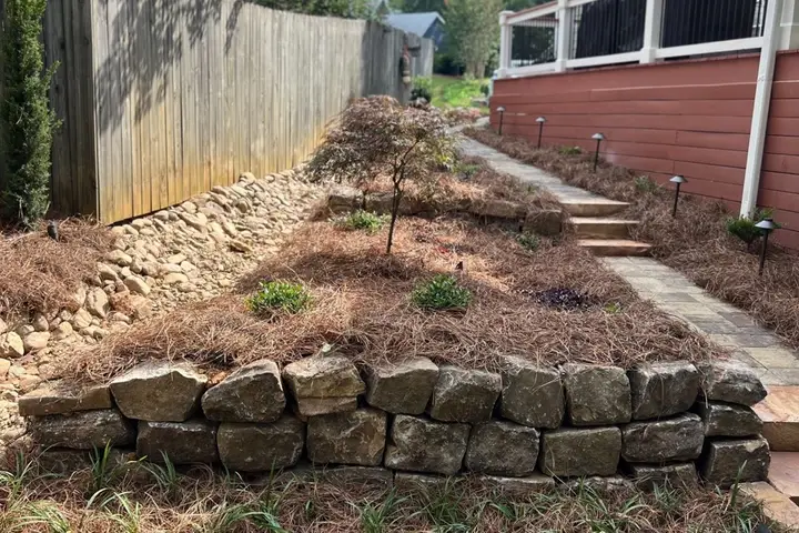 Tiered natural stone retaining wall with pine-straw planting beds, steps and path lights