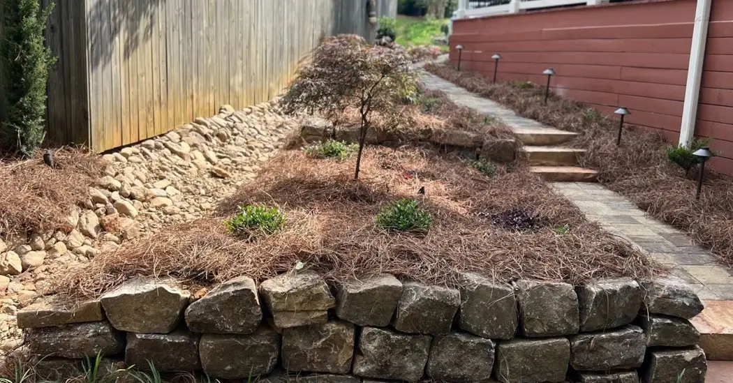 Tiered natural stone retaining wall with pine-straw planting beds, steps and path lights