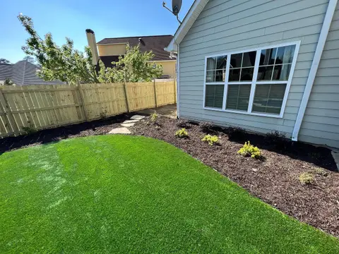 Turf lawn and mulched planting bed along a fence beside a house