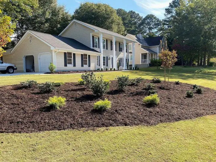 Green sod lawn and a new mulched shrub bed in front of a two-story house